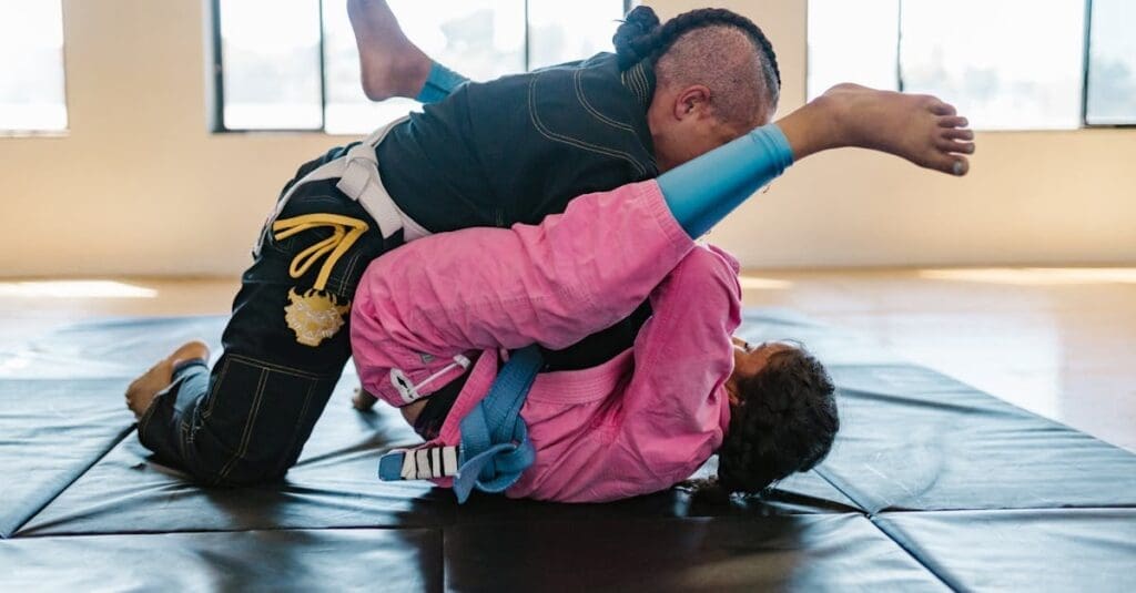 Two practitioners on a mat practicing ground-based teen self-defense skills, with one student using their legs to maintain distance and control.